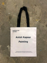 Load image into Gallery viewer, The back of the Anish Kapoor tote bag lying flat. The back is plain cotton with printed text reading "Modern Art Oxford Anish Kapoor Painting"