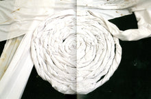 Load image into Gallery viewer, The inside of the book. Both pages are taken up by a double page spread of a photo of a close-up of an artwork. The piece features a tightly wound coil of twisted white fabric that is speckled with dirt.