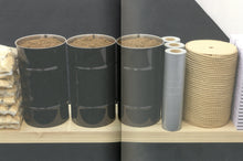 Load image into Gallery viewer, The inside of the book. Both pages feature a double-page spread of a photo of an artwork. The piece contains many elements such as barrels of dirt, stacked bags of gravel, rolls of tape, and a coil of rope, all arranged in a straight line.